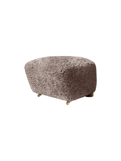 The Tired Man Ottoman upholstered in tactile Sahara sheepskin. The footstool has dark stained oak legs and brass castors.