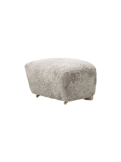 A Tired Man Ottoman footstool upholstered in light green Green Tea sheepskin, shown at an angle on a plain black background.