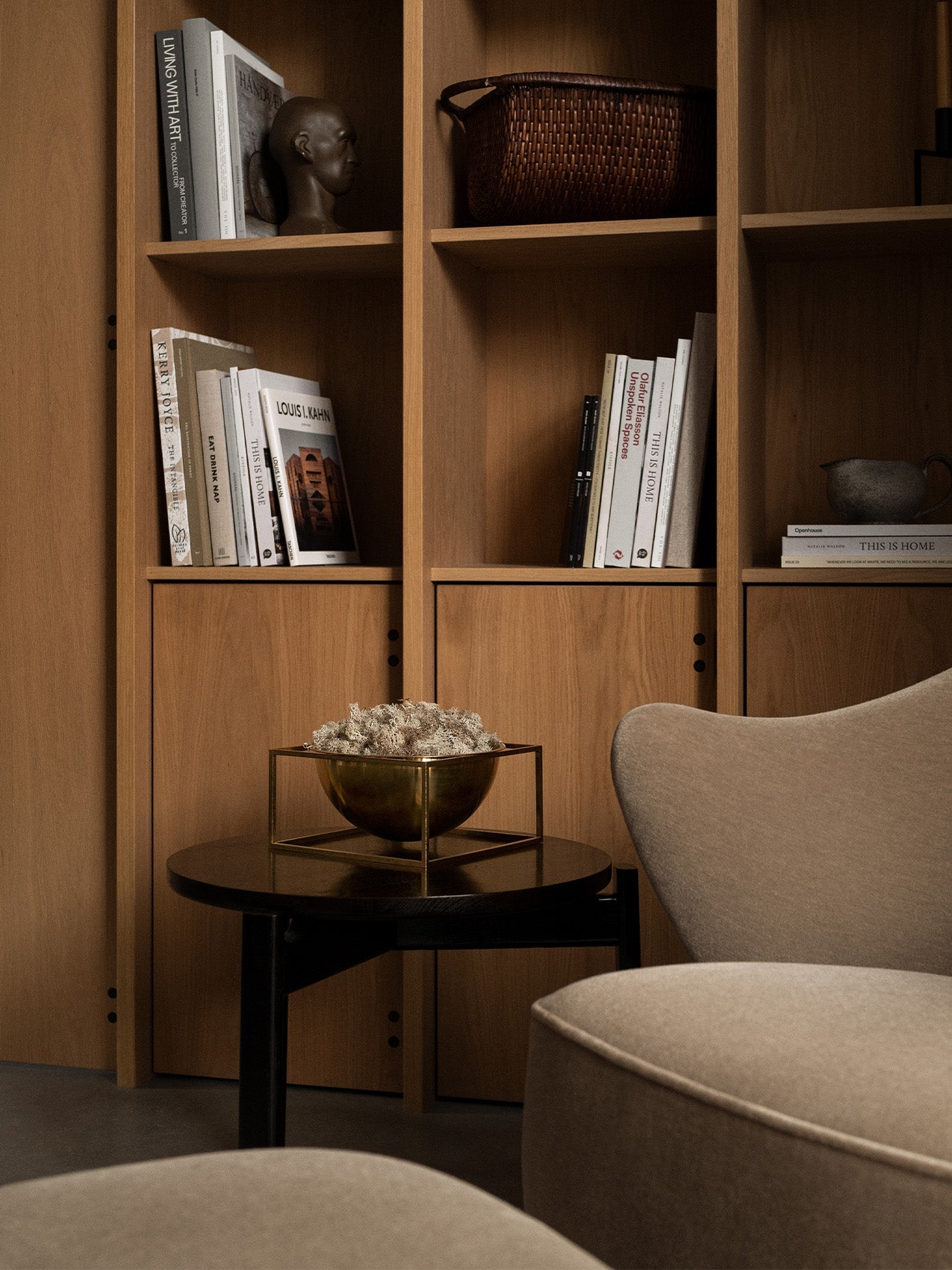 Brass Kubus Bowl Centerpiece Large on a dark side table, next to a beige Ingeborg Lounge Chair with a wooden bookcase behind.