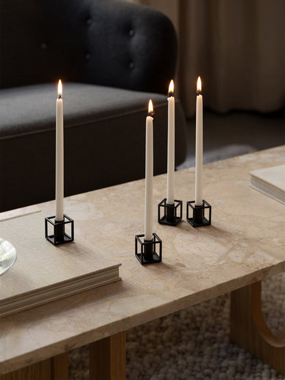 Four lit white candles in black Kubus Micro candle holders on a marble coffee table next to a book in a cosy living room.