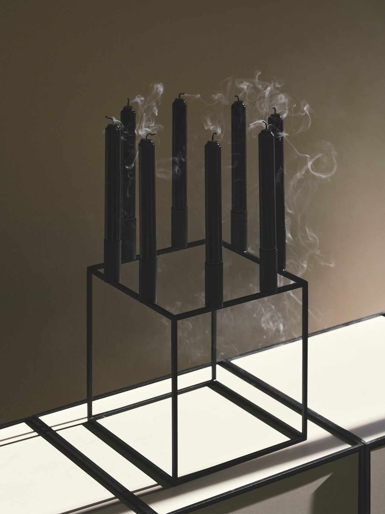 The minimalist Kubus 8 candle holder in black, holding eight black candles that have been extinguished, with smoke rising.