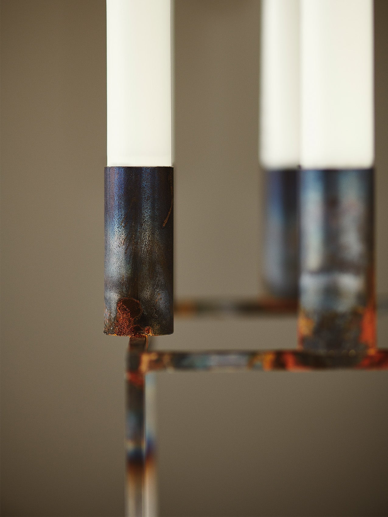 Close-up of the raw, patinated metal finish on the byLassen Kubus 8 candlestick, holding a simple white candle.