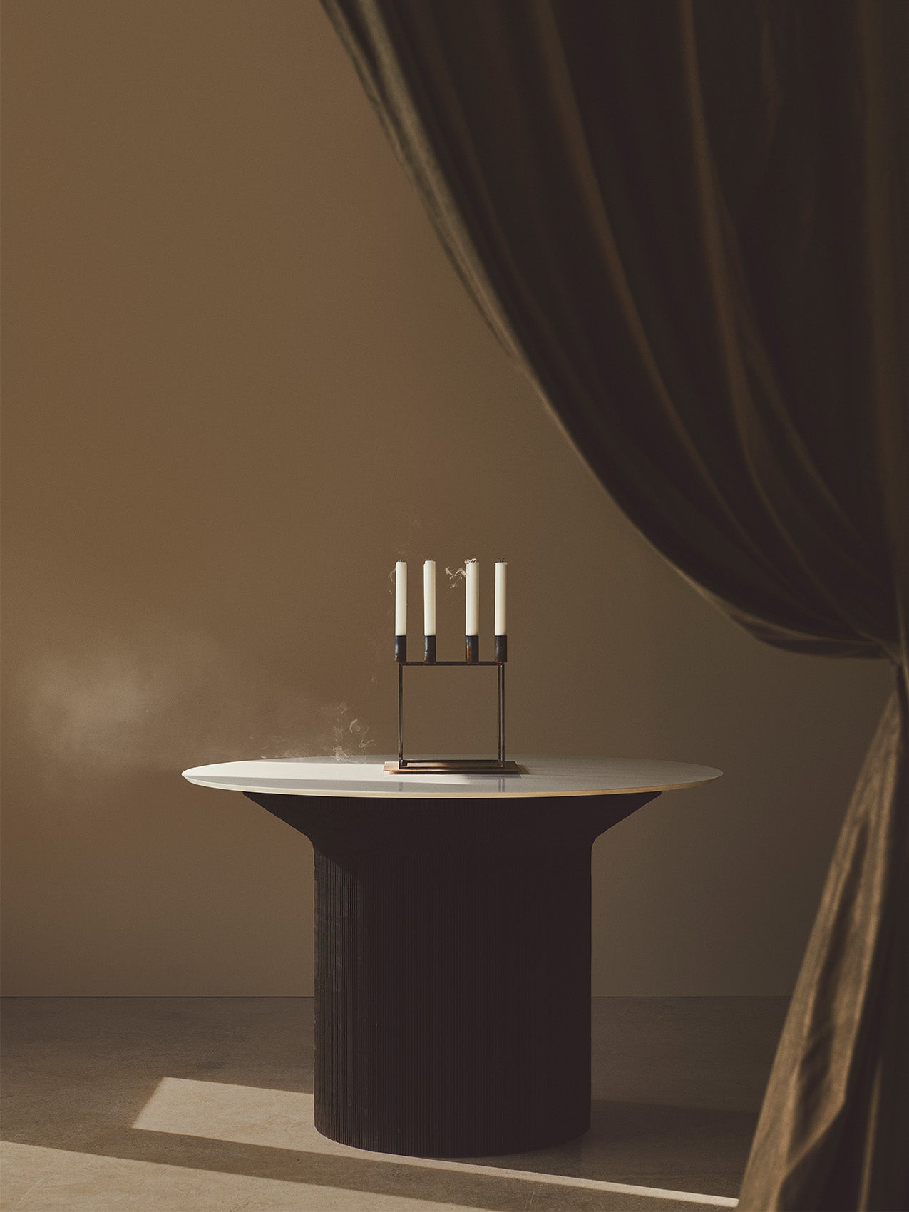 The by Lassen Kubus 8 candelabra with four extinguished, smoking candles on a contemporary table in a minimalist setting.