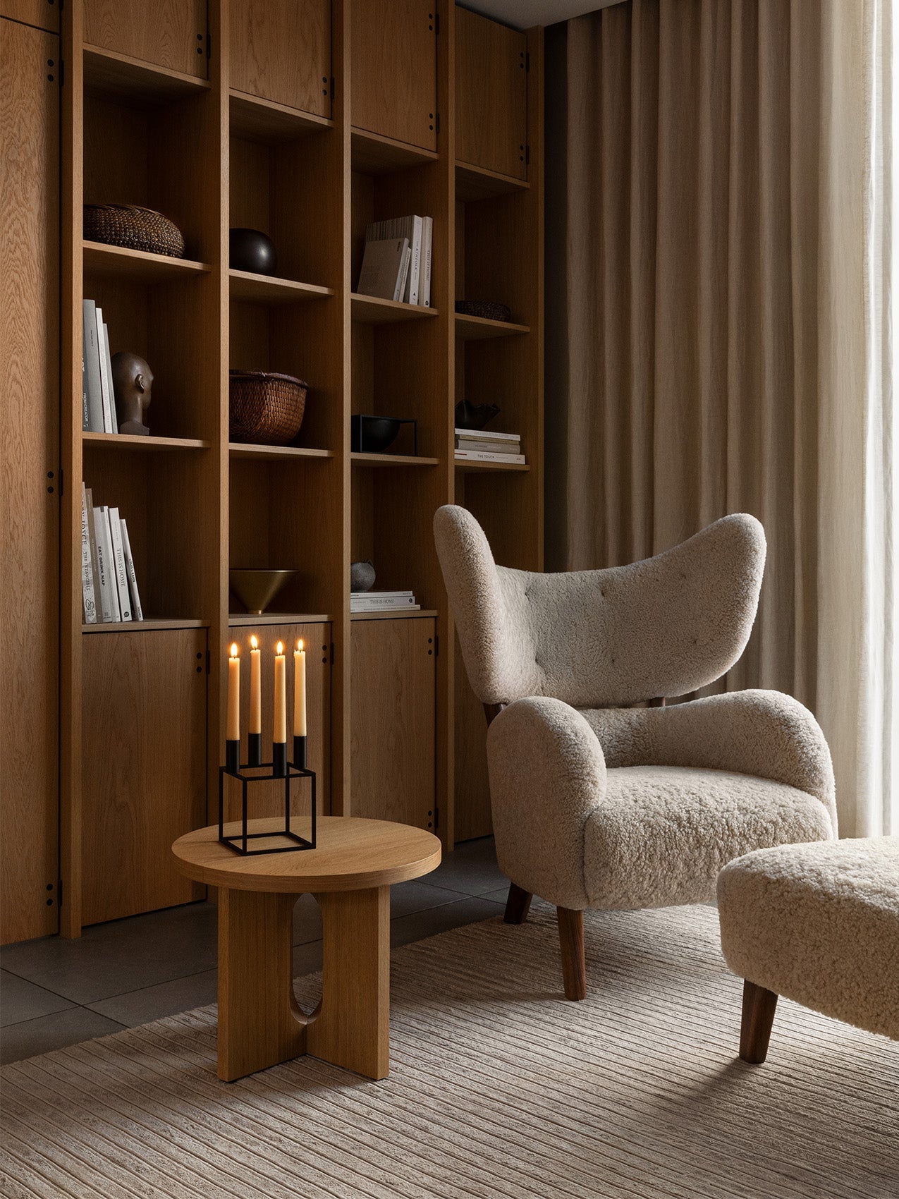 A cosy living room setting featuring the My Own Chair and footstool in cream sheepskin, beside a wooden bookcase and Kubus 4.