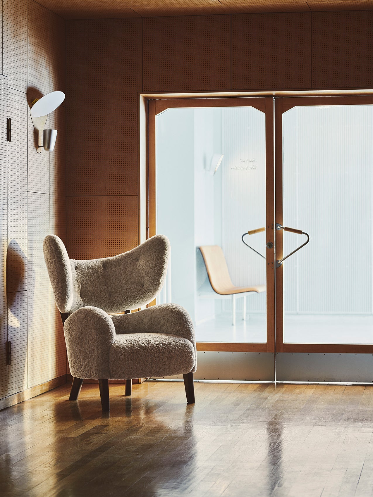 The My Own Chair in Sheepskin Moonlight sits in a sunlit corner with perforated wood walls and a polished wood floor.