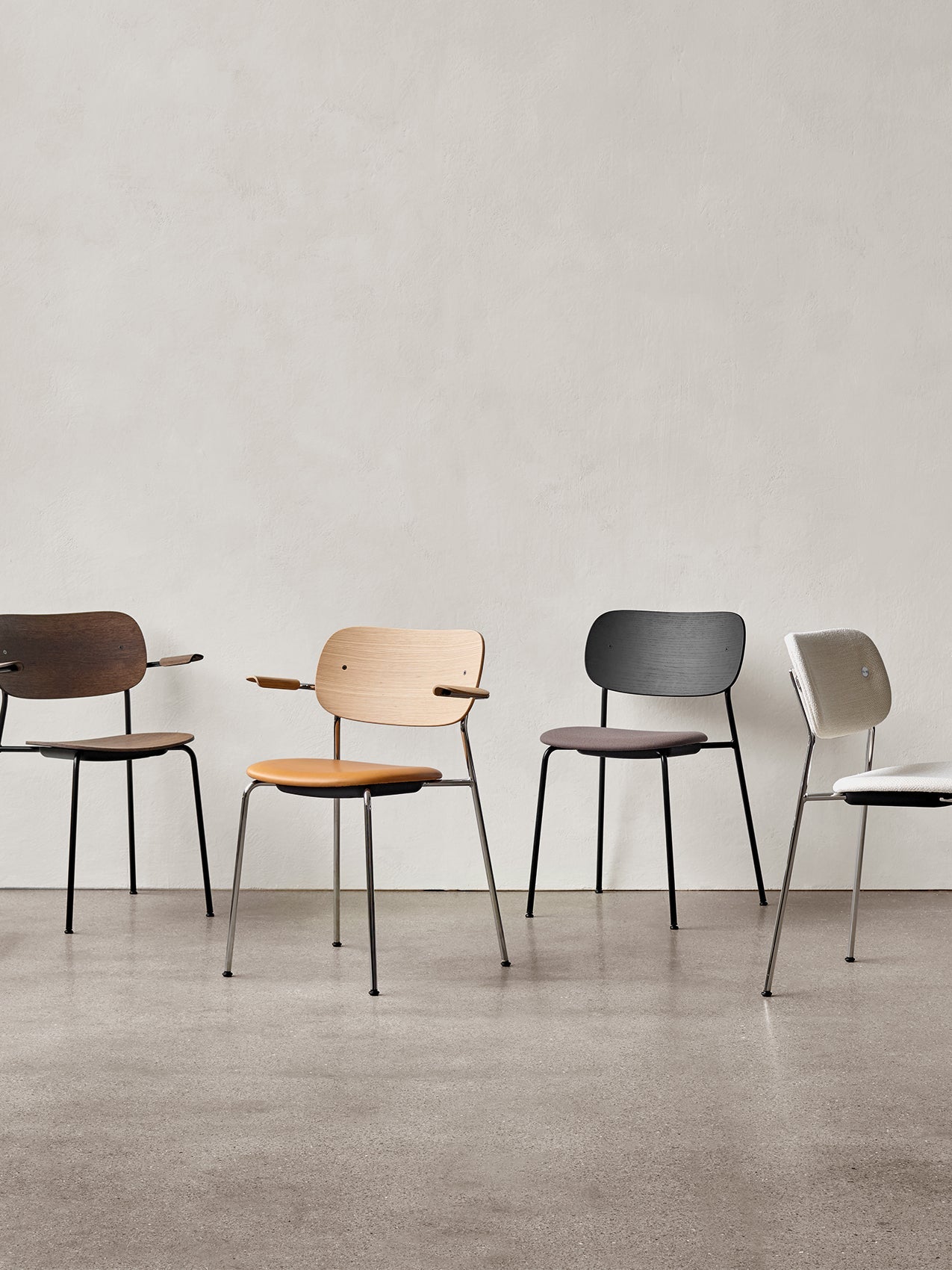 A lineup of four Co Dining Chairs in various finishes and upholstery options, both with and without armrests, against a wall.