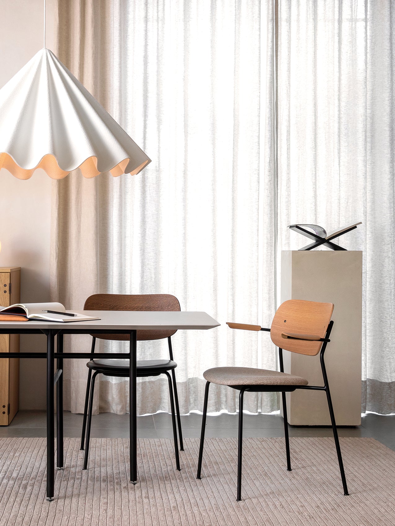 A dining scene featuring the Co Dining Chair with armrests and upholstered seat at a table beneath a large pendant lamp.