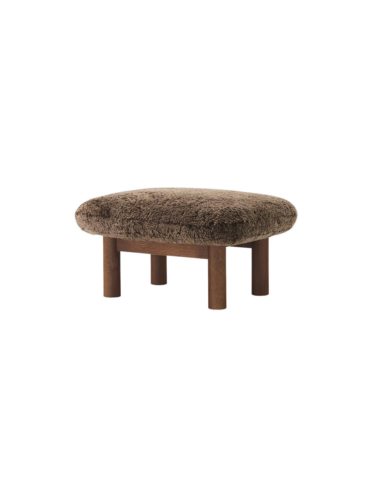 The Brasilia Ottoman with a fluffy brown sheepskin cushion on a dark stained oak base with four thick, cylindrical legs.