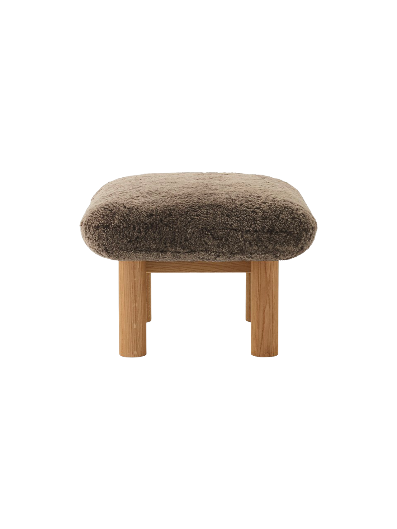 Side profile of the Brasilia Ottoman, featuring a thick, brown sheepskin cushion and robust cylindrical legs in natural oak.