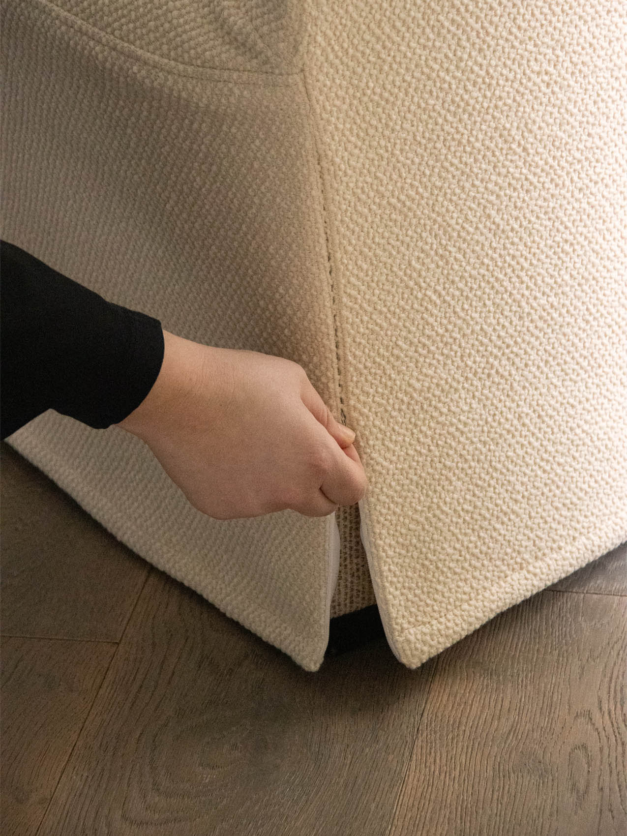 A close-up image showing a hand adjusting the cream-coloured, textured Tearoom Loose Cover at the base of the furniture.